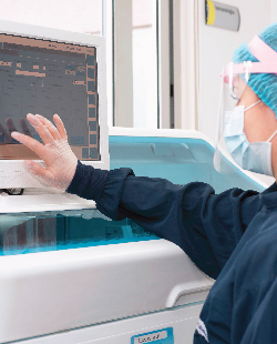 Se ve a una profesional de la salud usando tapabocas y una máscara protectora mientras manipula la pantalla de un equipo médico.